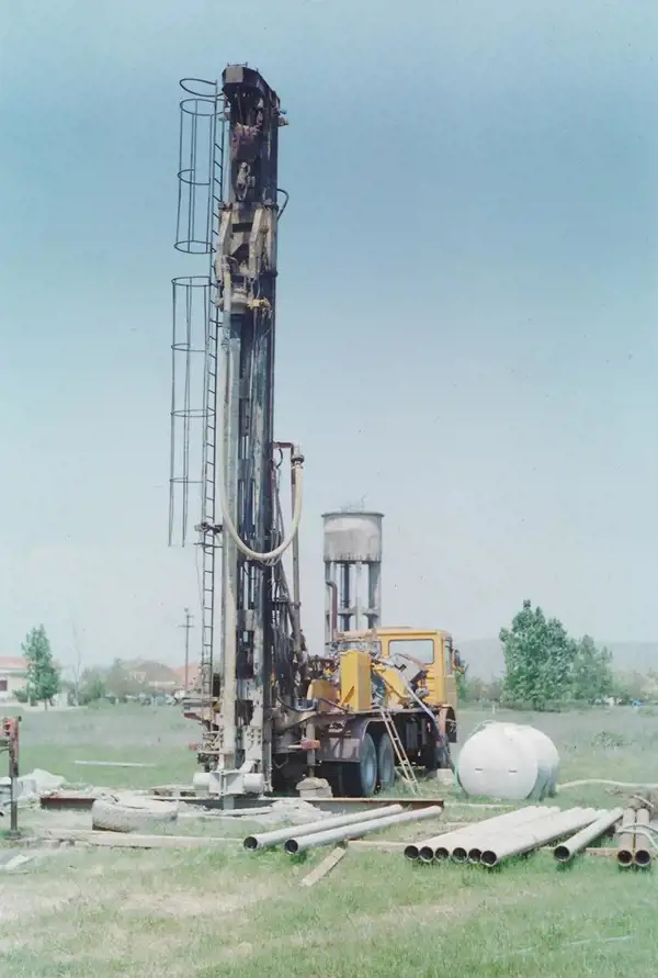 Truck-mounted drilling rig with raised mast at a water well site